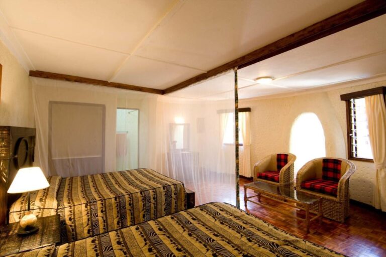 A twin room with beds under mosquito nets, and two armchairs with red checked cushions