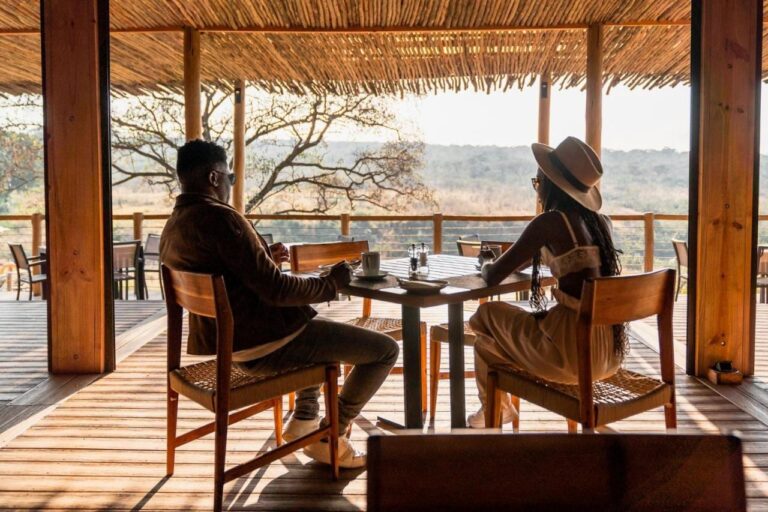 A couple at a table on the lodge's covered terrace, facing the bush