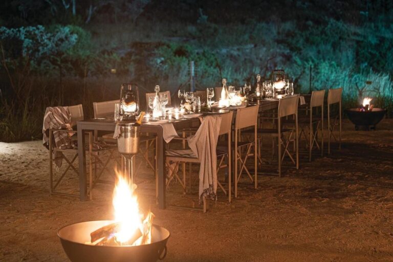 A long table set for dinner in the open air, among lanterns and fires in braziers