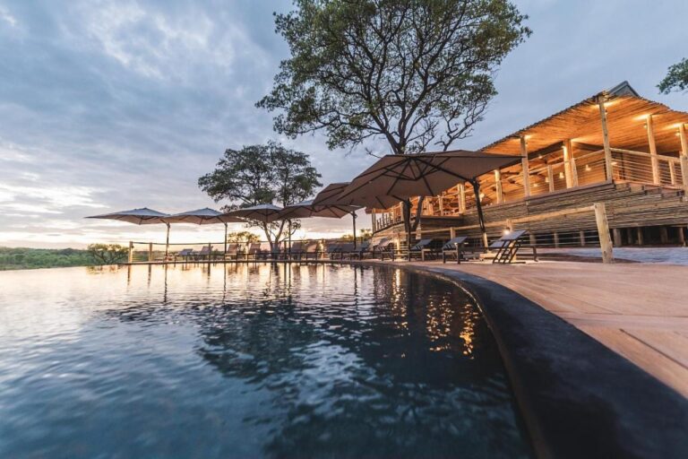The infinity pool of Mdluli Safari Lodge and its lit main building, under a cloudy sky