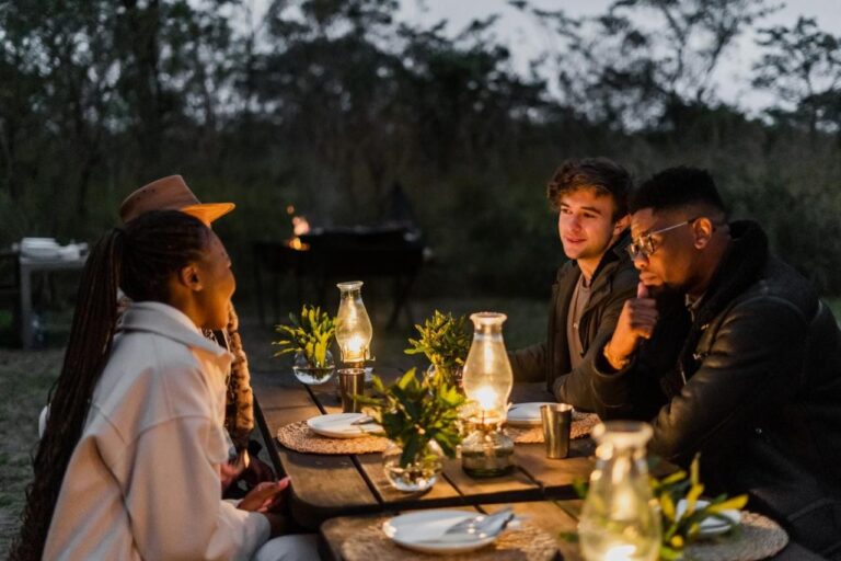 Diners at an outdoor table lit by oil lamps, at nightfall