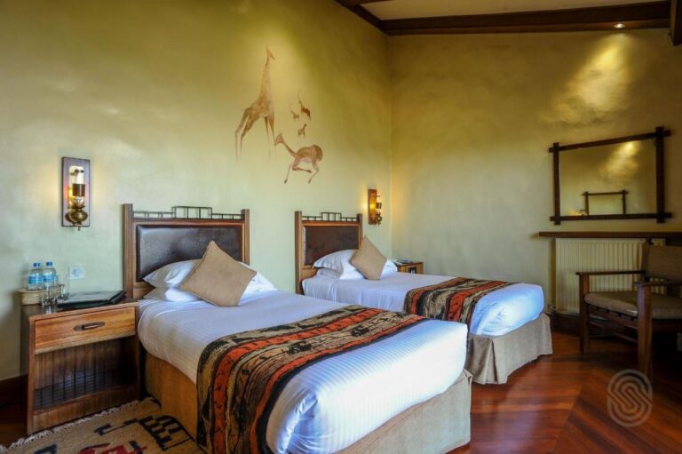 A twin room with a giraffe and antelopes painted on the wall