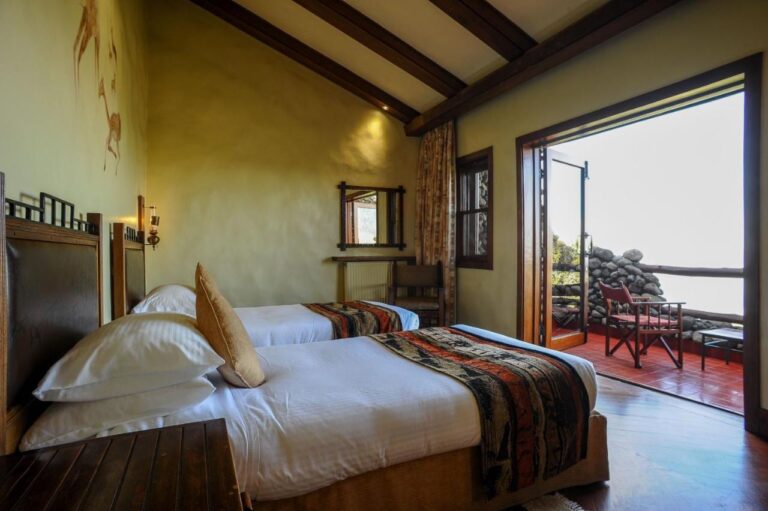 A room with two beds opening onto a balcony, with a red canvas armchair
