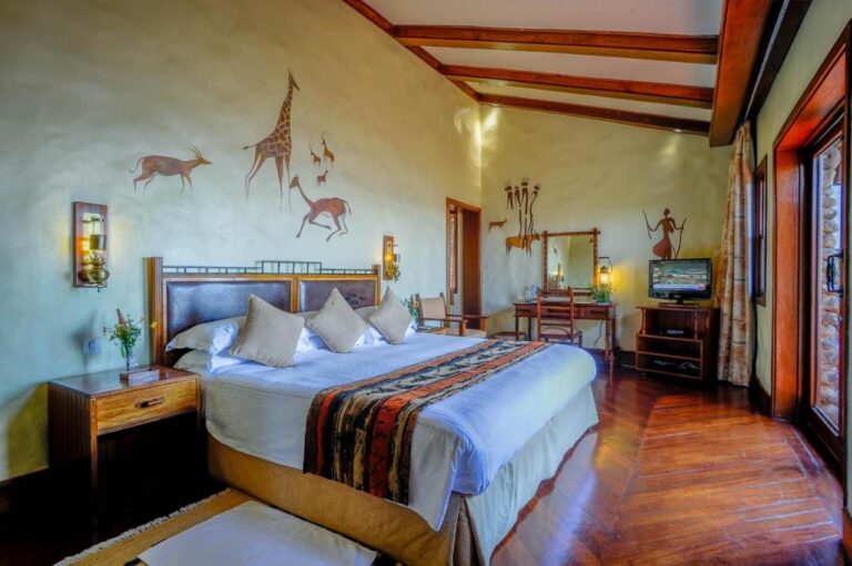 A room with a double bed, a desk, a TV and a giraffe painted on the wall