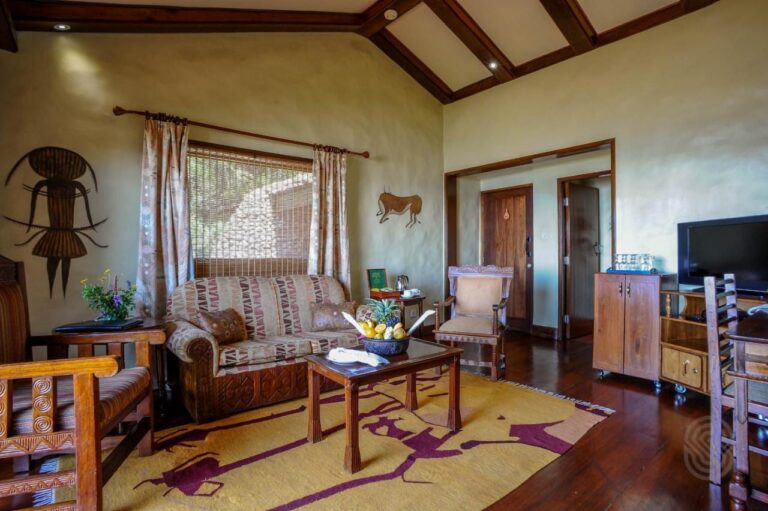 The living room of a suite, with carved wooden armchairs and a yellow patterned rug