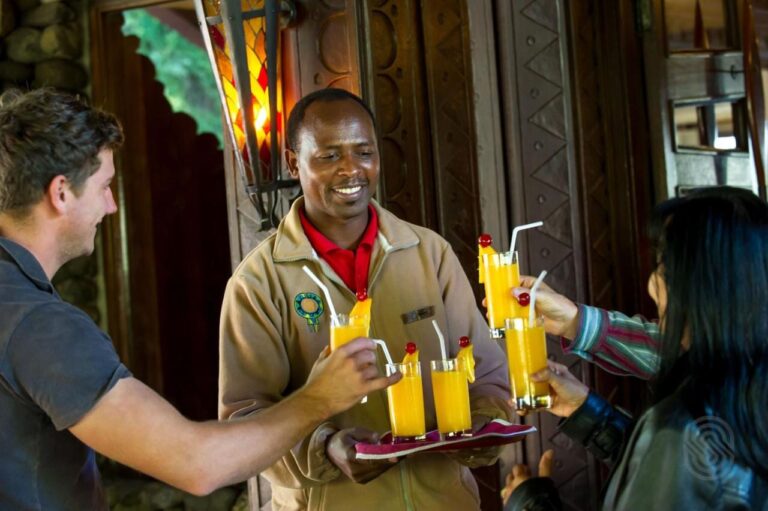 A Ngorongoro Serena Safari Lodge staff member offers a tray of fruit juice to two travelers