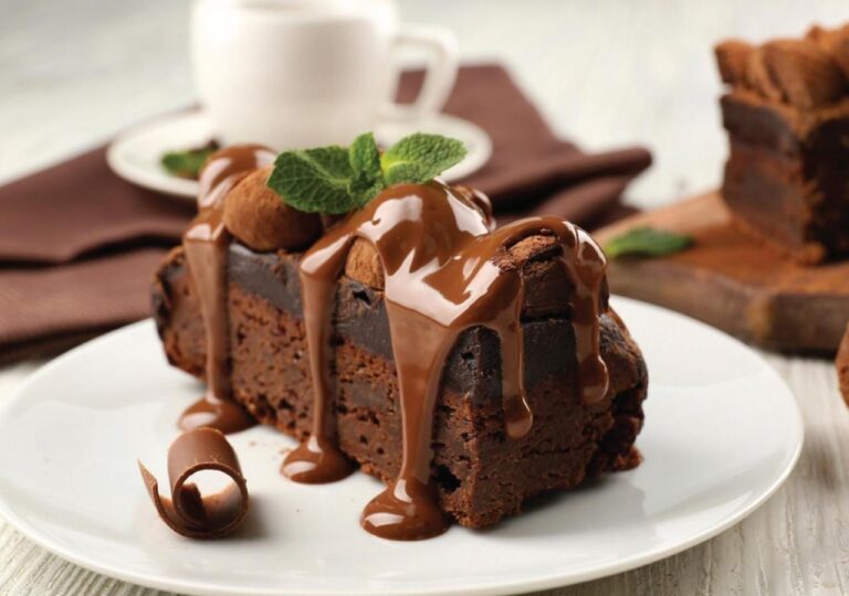 A slice of chocolate cake topped with sauce, with mint leaves