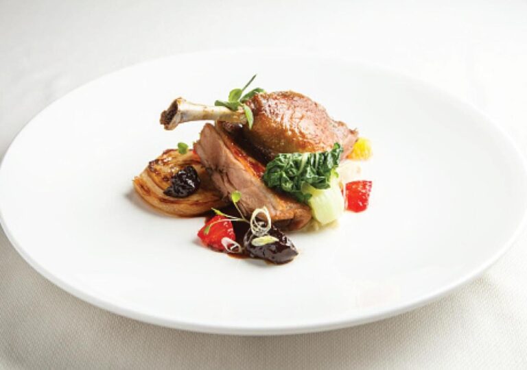 A roast poultry leg with its vegetables on a white plate