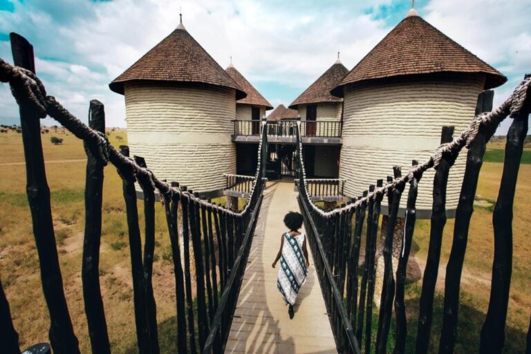 A woman walking along a walkway with rope railings, toward round towers with pointed roofs