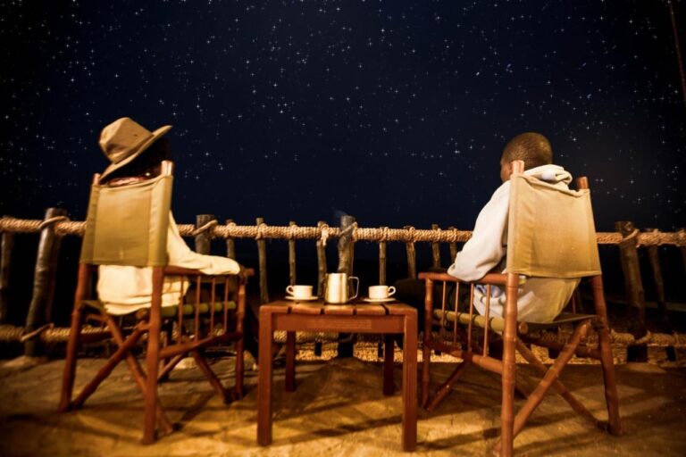 Two people sitting in canvas chairs on the terrace, two cups on the table, under a starry sky