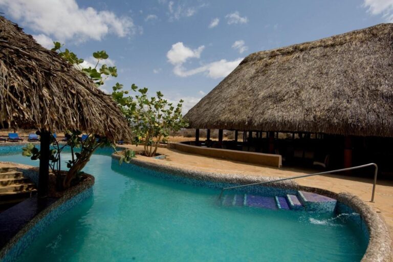 The blue mosaic pool, between a thatched shelter and a large thatched building