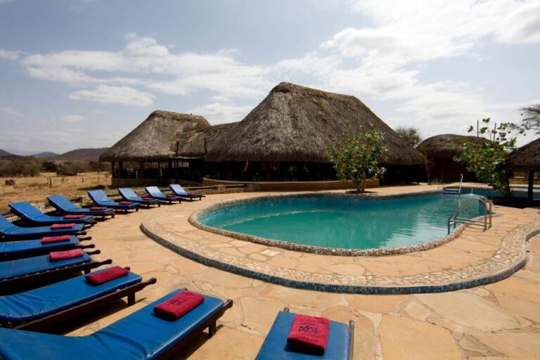 Blue sun loungers with red towels by the pool, in front of thatched buildings