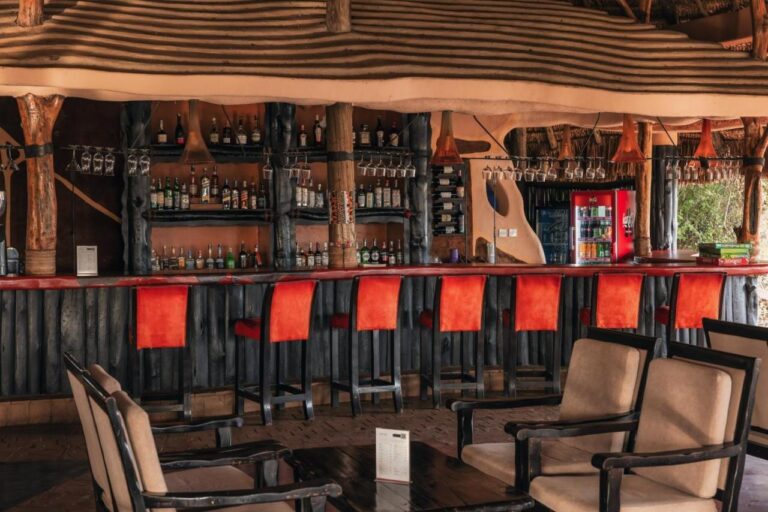 The bar, its red stools and shelves of bottles, with armchairs in the foreground