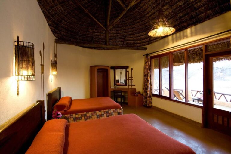 A twin room with orange bedspreads and large windows looking onto a terrace