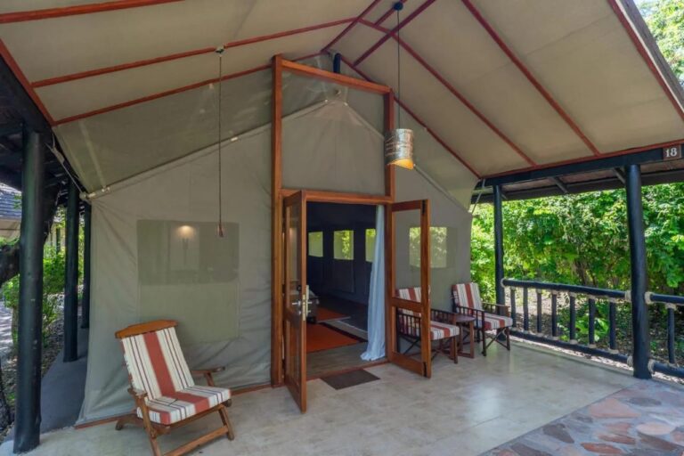 The entrance to a tent sheltered under a roof, with striped chairs on the veranda