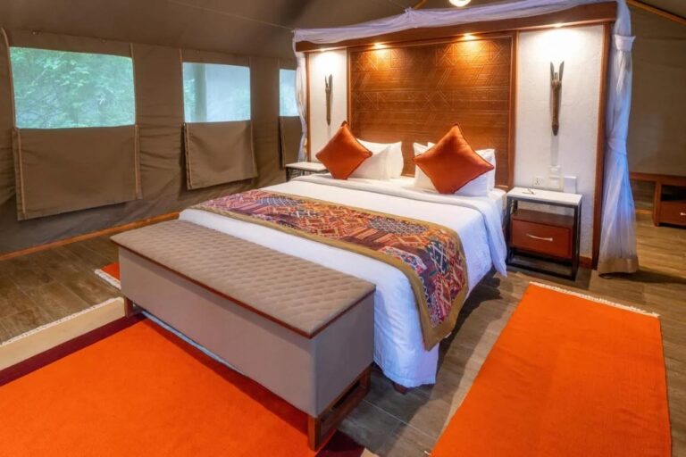 The bed of a tent seen at an angle, with its wooden headboard and orange rugs