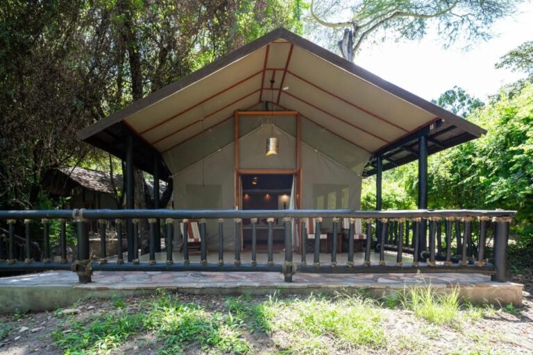 A Sarova Mara Game Camp tent under its roof, on a terrace with a railing, among the trees