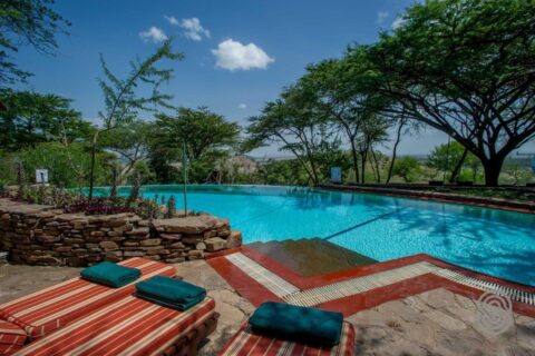 The infinity pool of Serengeti Serena Safari Lodge, with its red-striped sun loungers and green towels, under the acacias