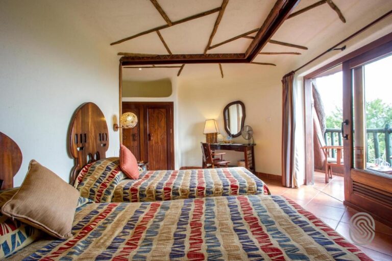 A room with two beds and cut-out wooden headboards, opening onto a balcony through a glass door