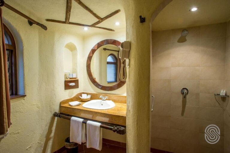 A bathroom with stucco walls, a washbasin under a round mirror and a large tiled shower