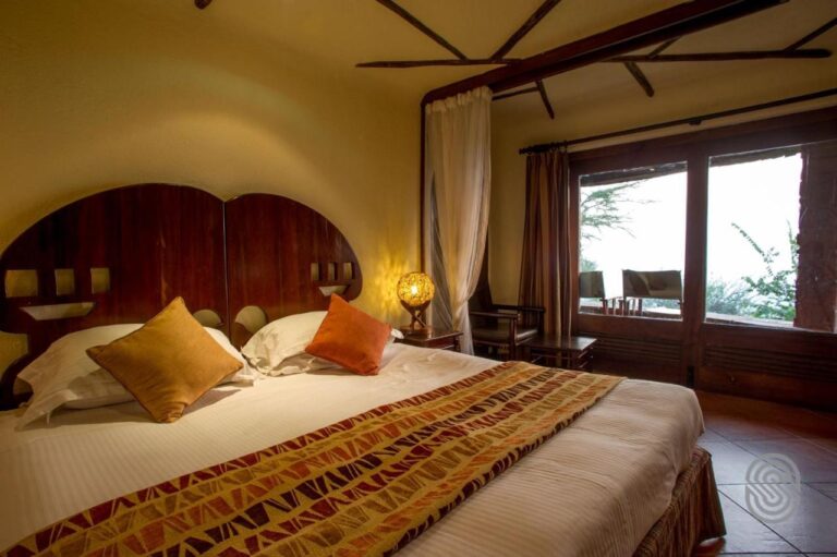 A double bed with white sheets and orange cushions, under a rounded wooden headboard