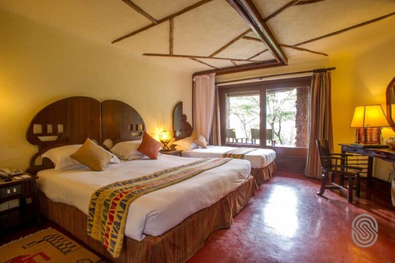 A room with a double bed and a single bed with cut-out wooden headboards, and a desk by the window