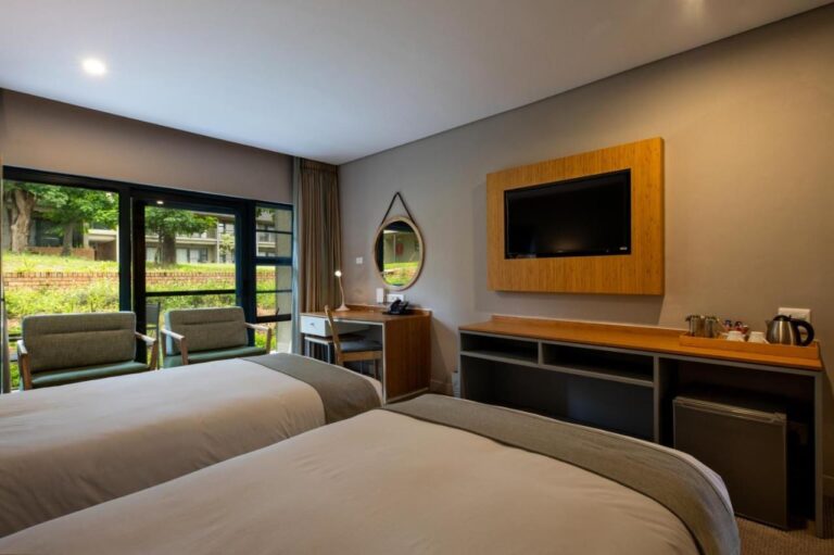 A room with two beds, a TV, a kettle and a view of the garden