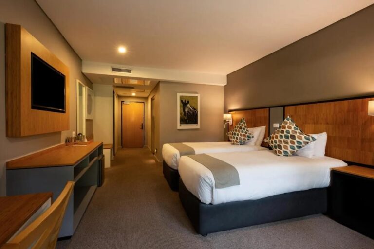 A room with two beds, seen from the TV and desk side, with a photo of a zebra on the wall