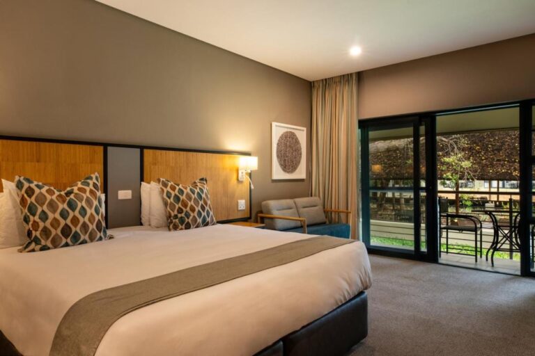 A room with a double bed and a sofa, opening onto a furnished balcony