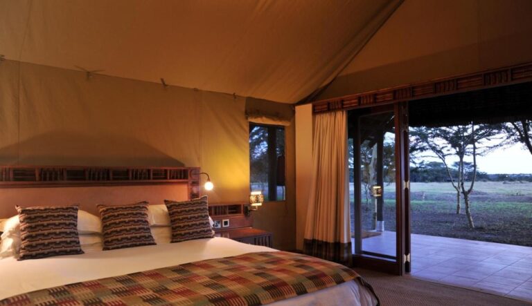 A large bed next to a picture window open onto a terrace and the plain