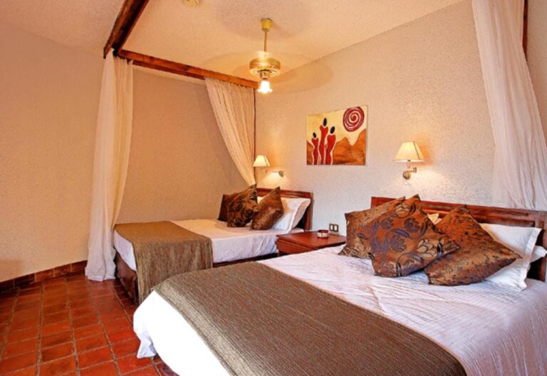 A room with two beds, sheer curtains and a ceiling fan