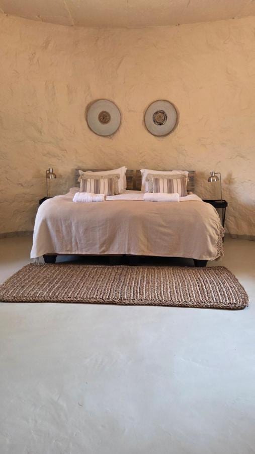 A room with rounded, plastered walls, a double bed, two decorative discs on the wall and a woven rug