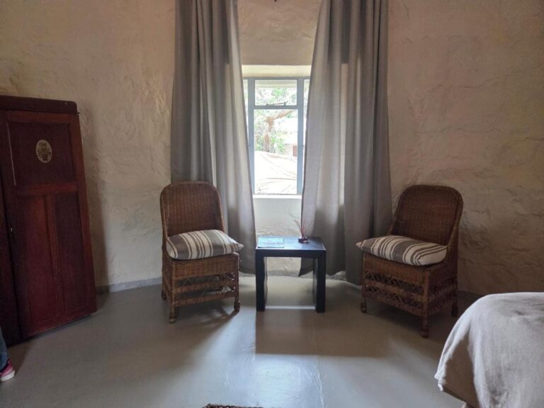 Two rattan armchairs and a small table in front of a window with gray curtains, next to a wooden wardrobe