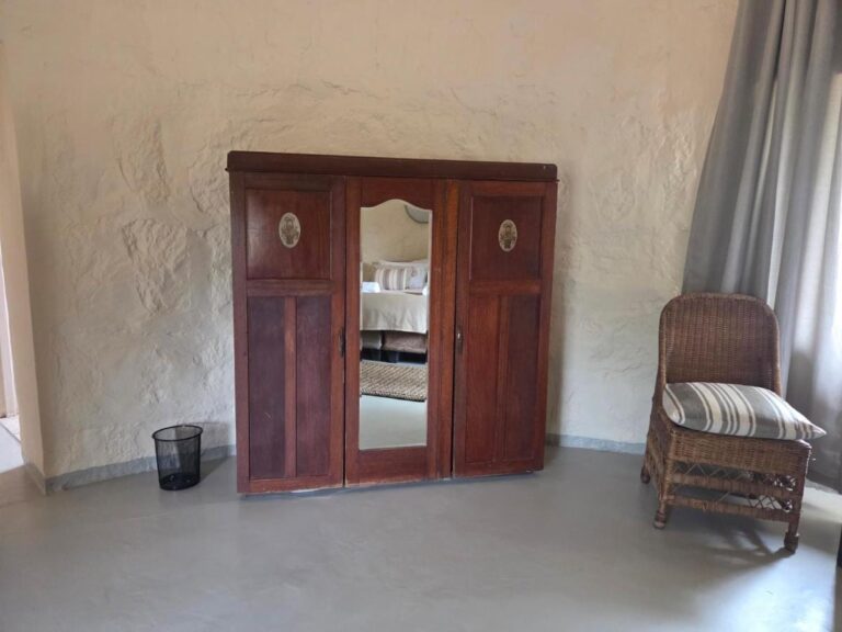 A dark wood wardrobe with a mirrored door, and a rattan armchair, in a room with plastered walls