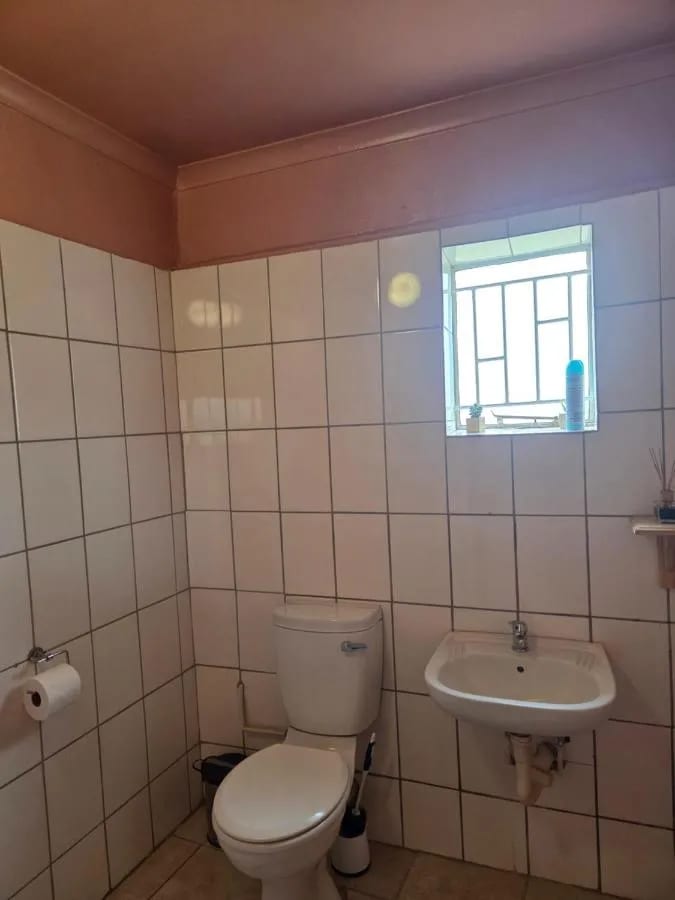 A white-tiled bathroom with a toilet, a sink and a small window