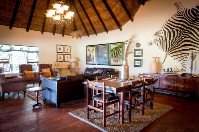 A lounge under the thatch, with leather sofas, a dining table and a zebra skin on the wall