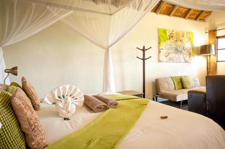 A bed under a mosquito net, with a towel peacock on the duvet and a photo of a young leopard on the wall