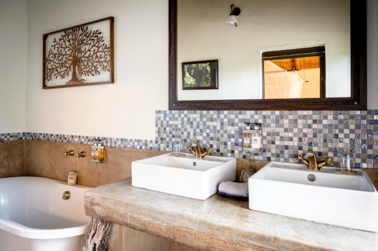 A bathroom with two sinks on a concrete counter, a bathtub and a mosaic backsplash