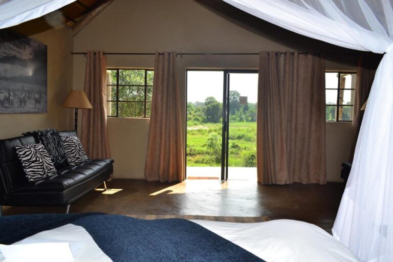 A room opening onto the green bush through a glass door, with a black leather sofa and zebra-print cushions