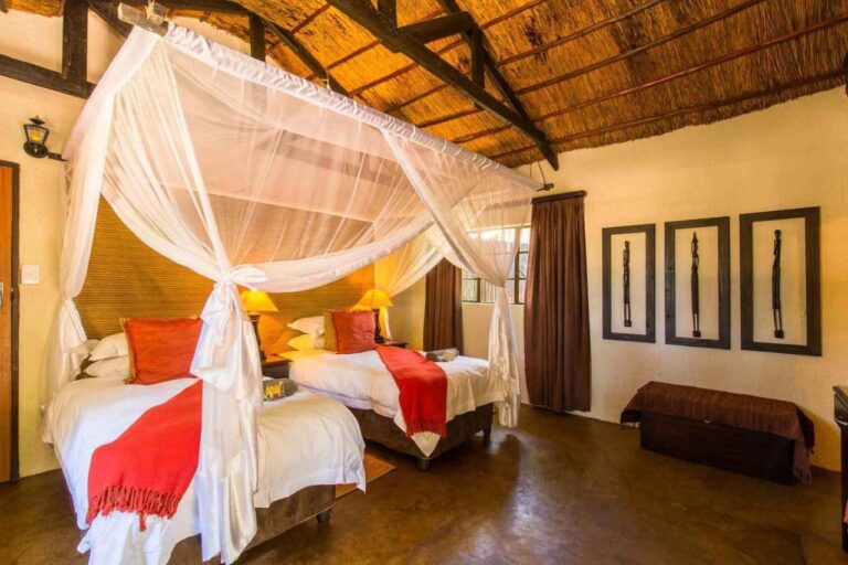 A room with two beds under mosquito nets, red throws and three frames on the wall