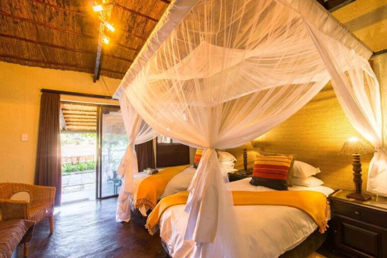 A room with two beds under mosquito nets, yellow throws and a glass door open onto the terrace